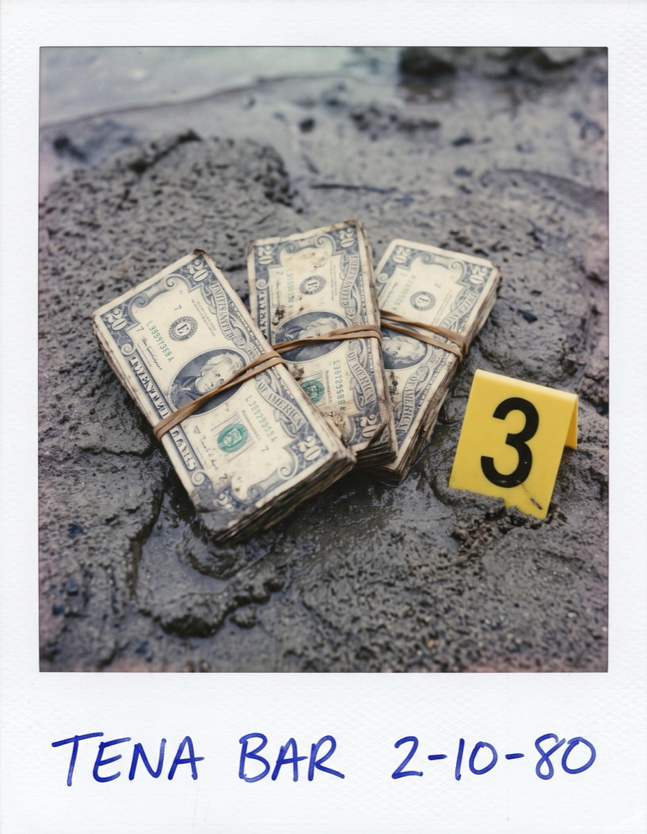 Polaroid of three banded bundles of twenty-dollar bills in wet river sand beside evidence marker 3, captioned Tena Bar 2-10-80.